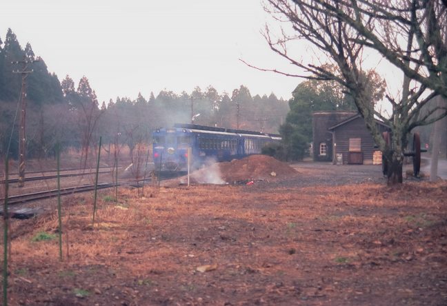 青いDC急行「えびの」と大畑駅の給水塔・保線小屋を眺める
