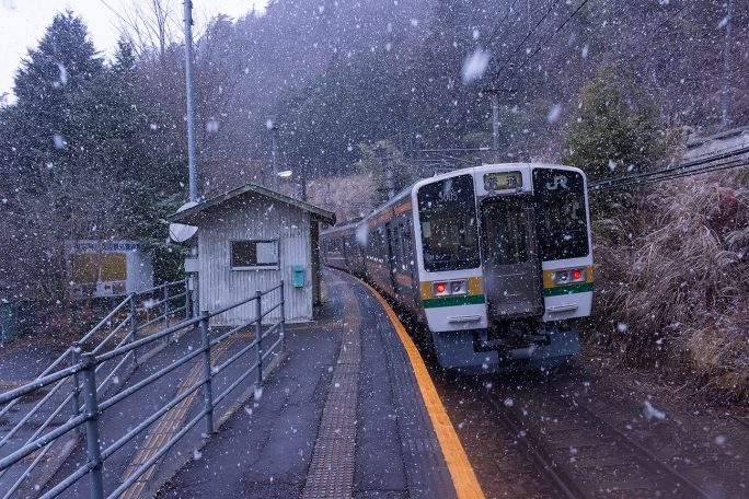 深々と降り続く雪の中出発していく普通列車を見送る