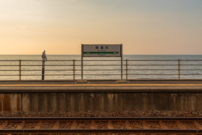 穏やかな夏の夕暮れの海をバックに佇む青海川駅の駅名標
