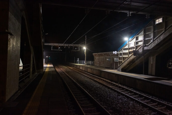 跨線橋の下で強風を避けながら夜の青海川駅を撮影する