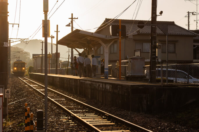 朝日がまぶしい湯田村駅で列車の到着を待つ高校生