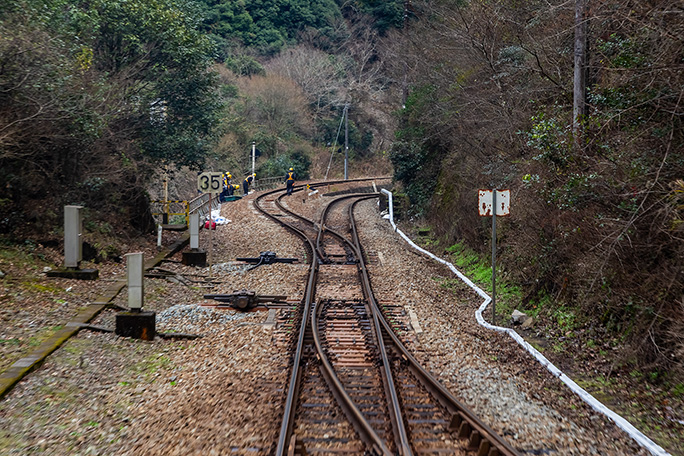 本線に入って加速していく普通列車の後尾から駅構内を見送る