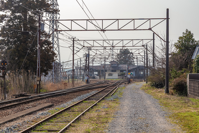 砂利道の集落道を辿ると留置線と本線の向こうに枝分かれしていく線路と旧待合室の建物が見えてくる